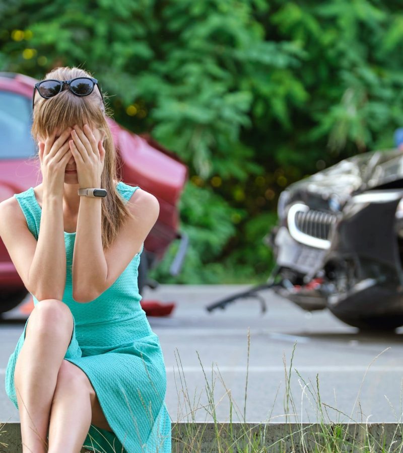 Stressed woman driver sitting on street side shocked after car accident. Road safety and insurance